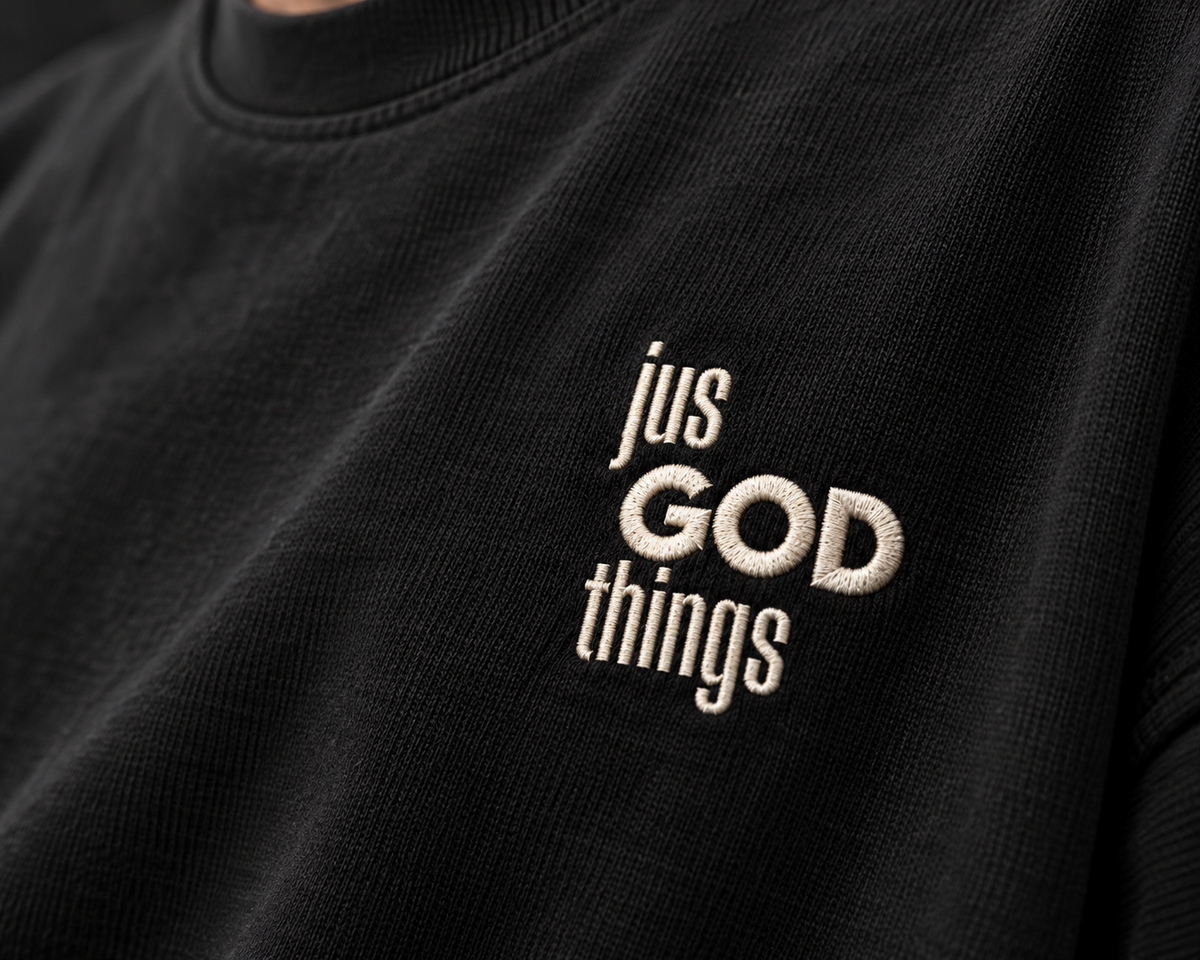Close-up of the off-white Jus God Things chest embroidery on black T-shirt fabric.