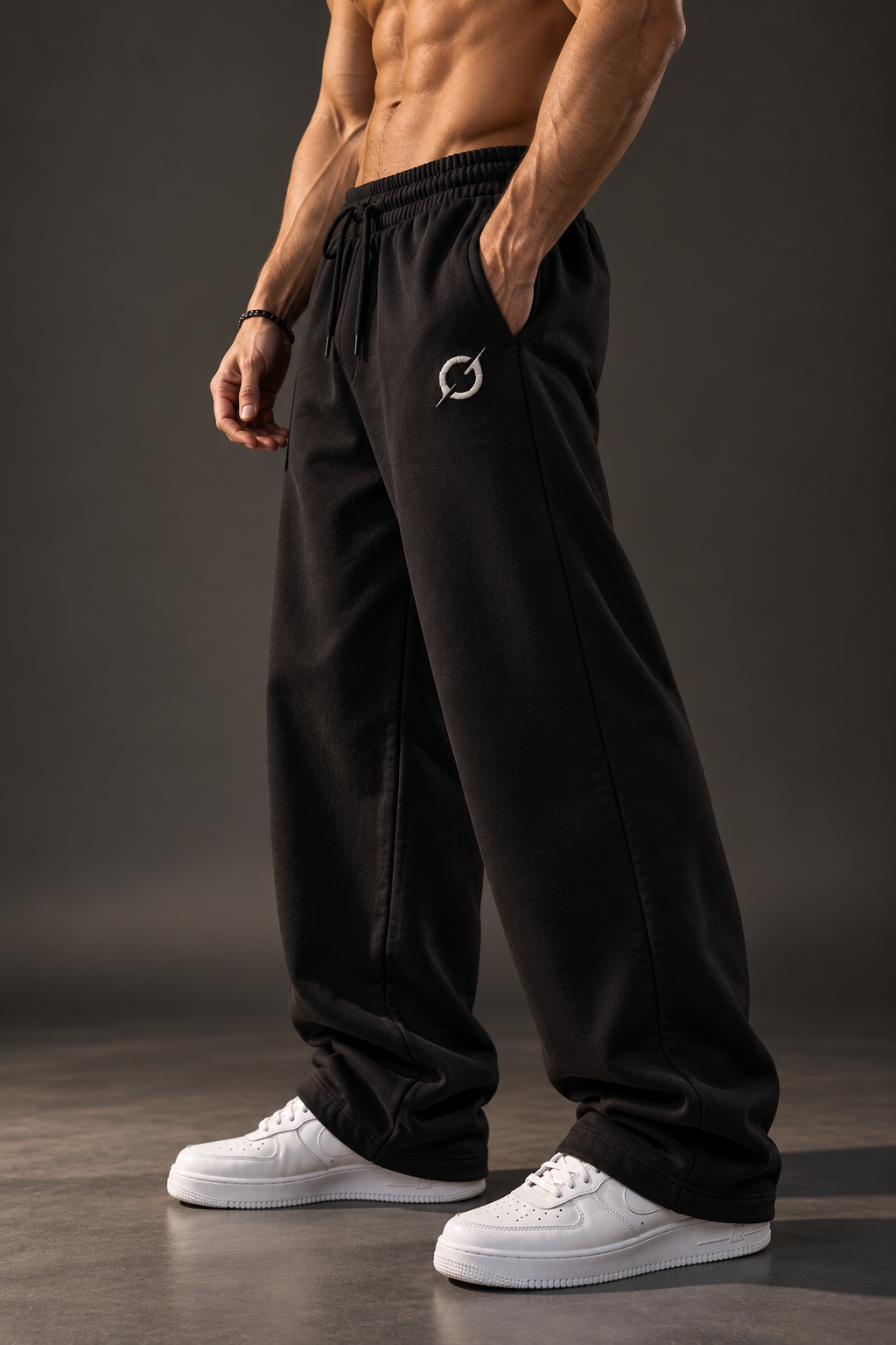 Close-up of black JGT relaxed-fit sweatpants showing the loose leg silhouette, embroidered logo and casual styling.