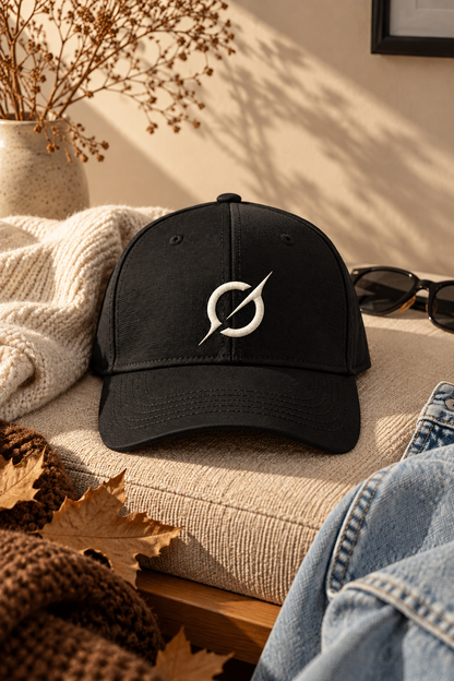 Black JGT baseball cap featuring off-white embroidered branding, displayed on a neutral sofa in warm natural light.