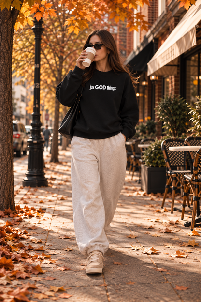 Model wearing a black JGT oversized sweatshirt with white chest branding, styled with beige trousers for a casual streetwear look.