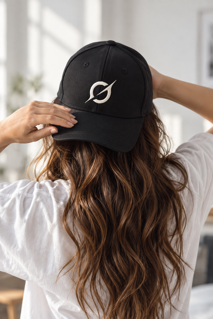 Woman wearing a black JGT baseball cap with an off-white embroidered circular logo, adjusting the cap while wearing a white T-shirt indoors.
