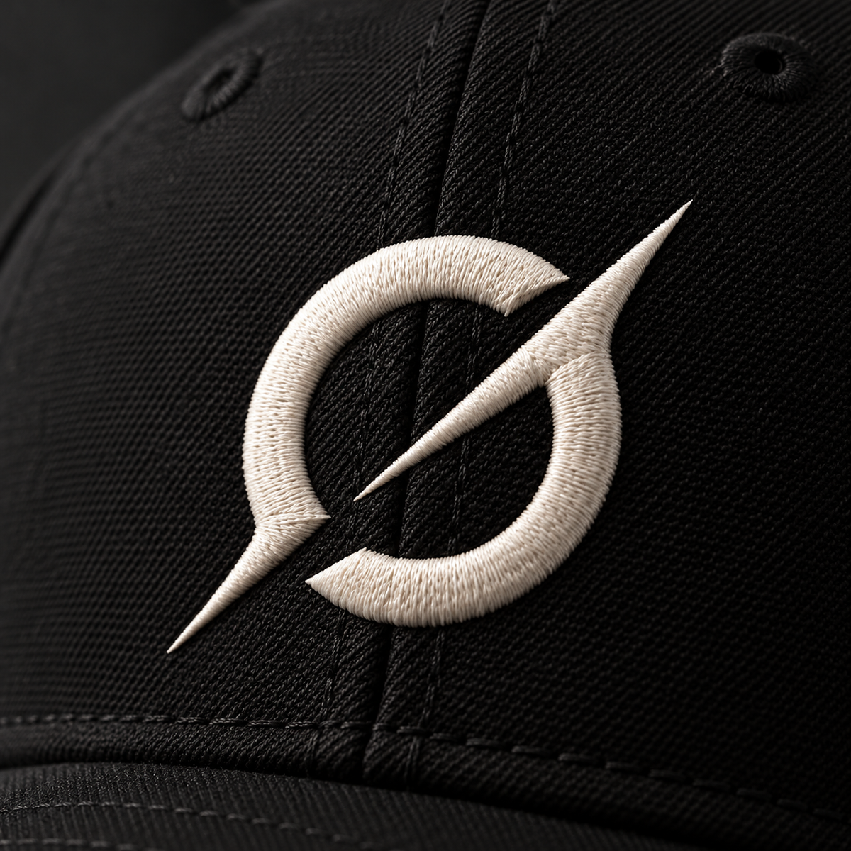 Close-up of the off-white embroidered JGT logo on the textured black fabric of a baseball cap.