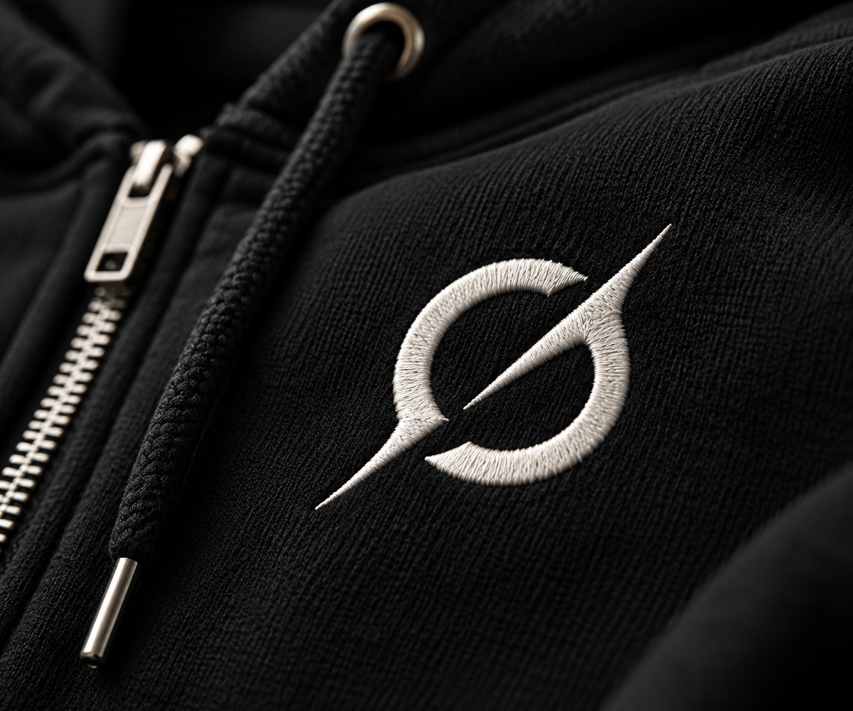 Close-up of the off-white JGT logo on black heavyweight zip-up hoodie fabric beside the metal zipper.